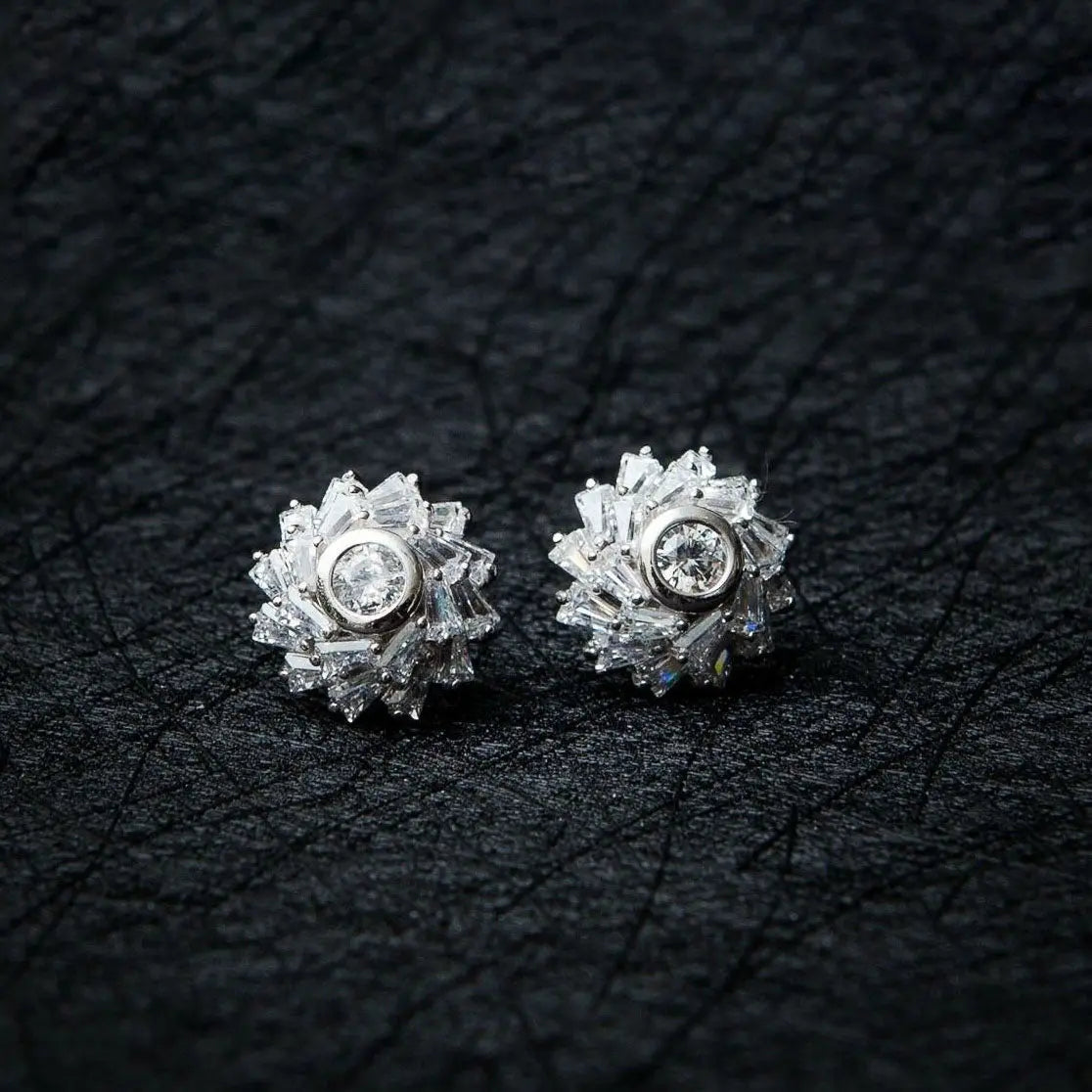 A pair of sterling silver stud earrings featuring a cubic crystal star flower design, set on a black textured background.